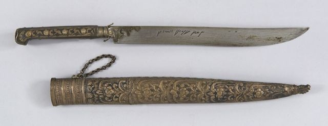 Poignard ottoman dit bishaq. Poignée en métal argenté niellé. Lame à dos plat avec écritures. Fourreau recouvert de métal argenté à...