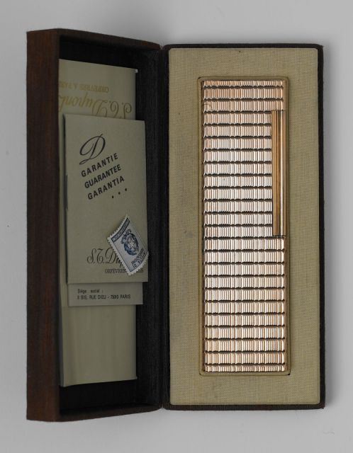 DUPONT, Briquet de table plaqué or à décor ligné. Parfait état de fonctionnement. Etat proche du neuf, avec boite. 14 x 4 x 1,8 cm.